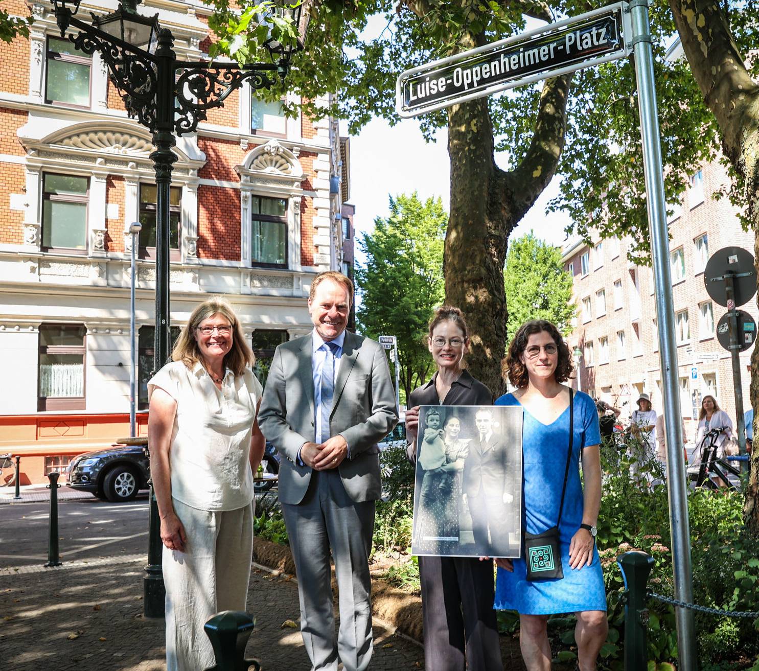 Das Straßenschild für den Luise-Oppenheimer-Platz wurde gemeinsam von (v. l.) Bezirksbürgermeisterin Annette Klinke, OB Dr. Stephan Keller sowie den Enkelinnen von Luise Oppenheimer, Linda Green und Catherine Green-Anthony, enthüllt.