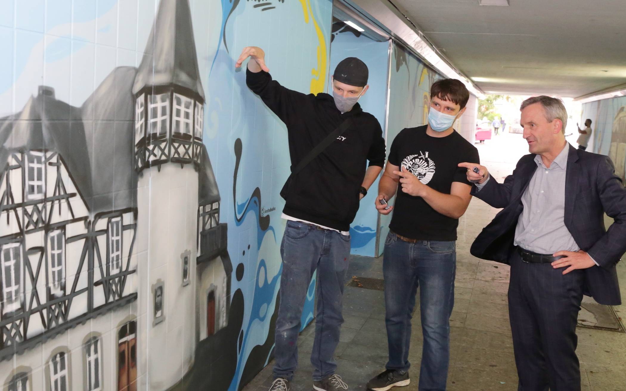  Die beiden Graffiti-Künstler Alex Weigandt und Jaroslaw Masztalerz präsentieren OB Thomas Geisel ihre Kunstaktion, hier ein Motiv von Schloss Eller. Foto: Stadt/ Ingo Lammert 