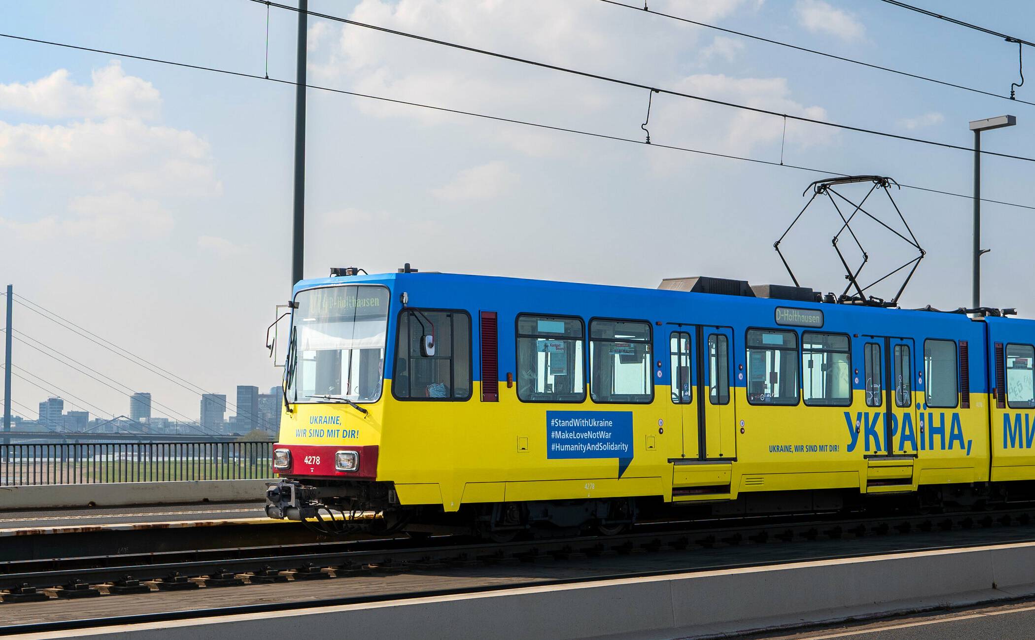   „УКРАЇНА, МИ З ТОБОЮ!“ – „Ukraine, wir sind mit Dir!“ Die Rheinbahn zeigt „Flagge“. Die aktuelle im Hochflurnetz fahrende  Bahn ist komplett in die ukrainischen Landesfarben, versehen mit der Solidaritätsbekundung in Landessprache – ergänzt durch Hashtags, die für Frieden und Menschlichkeit werben.   