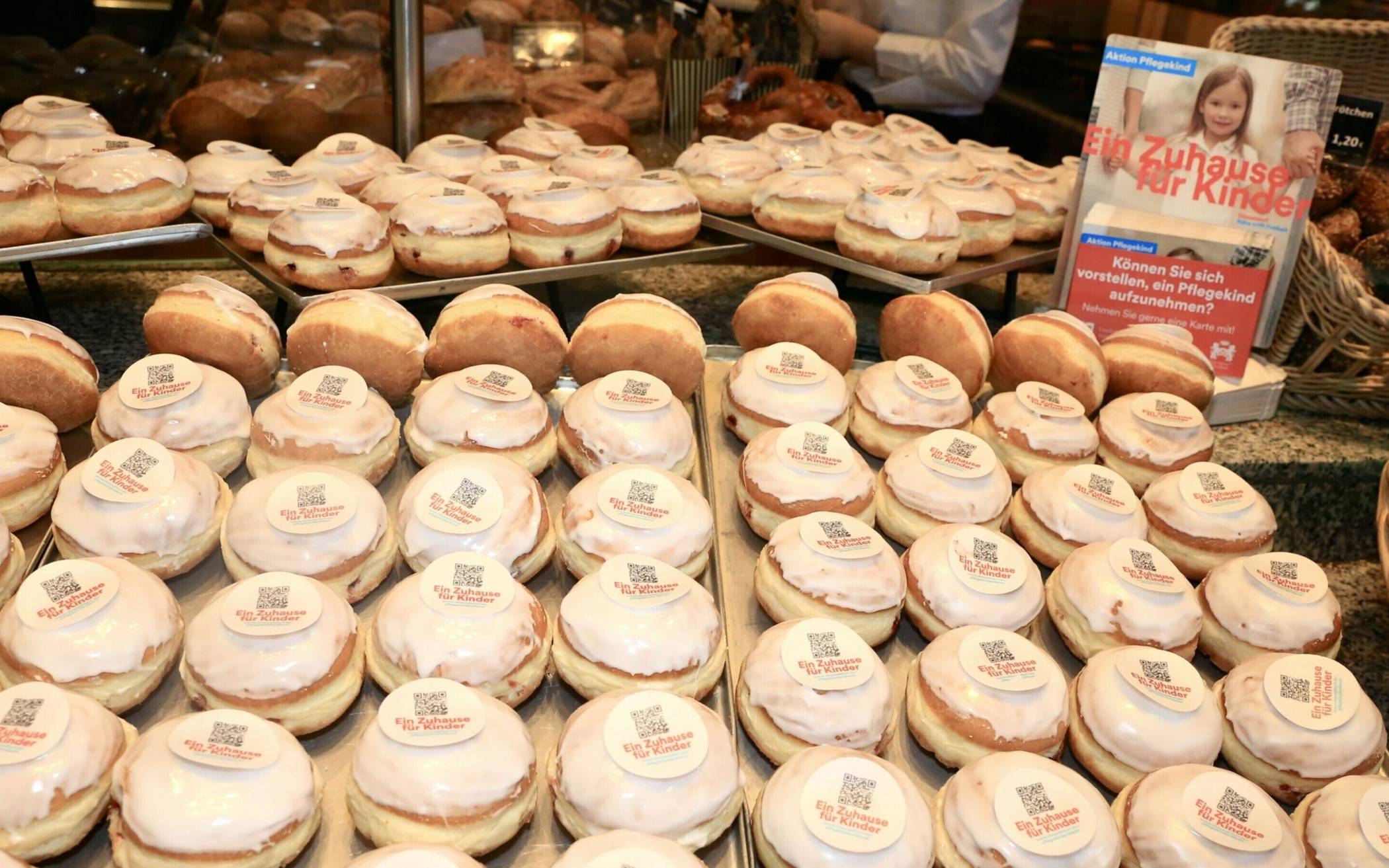  Um nach Pflegefamilien und Pflegeeltern zu suchen, werden in den Bäckereien aktuell etwa „Berliner“ mit aufgedrucktem QR-Code verkauft. 