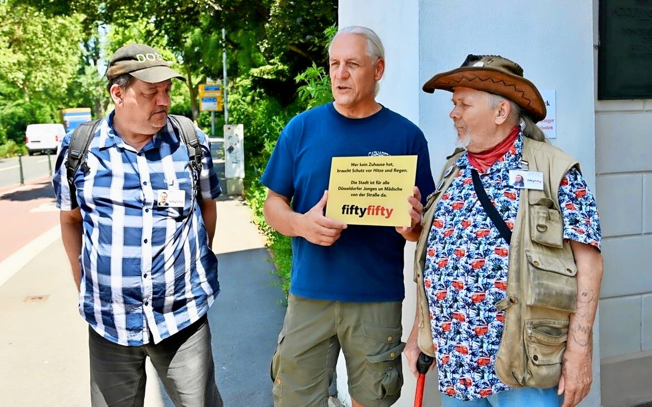  Helmut (v. l.) vom Straßenmagazin fiftyfifty, Streetworker Oliver Ongaro und Django hängen ein neues Schild am Ratinger Tor auf. 
