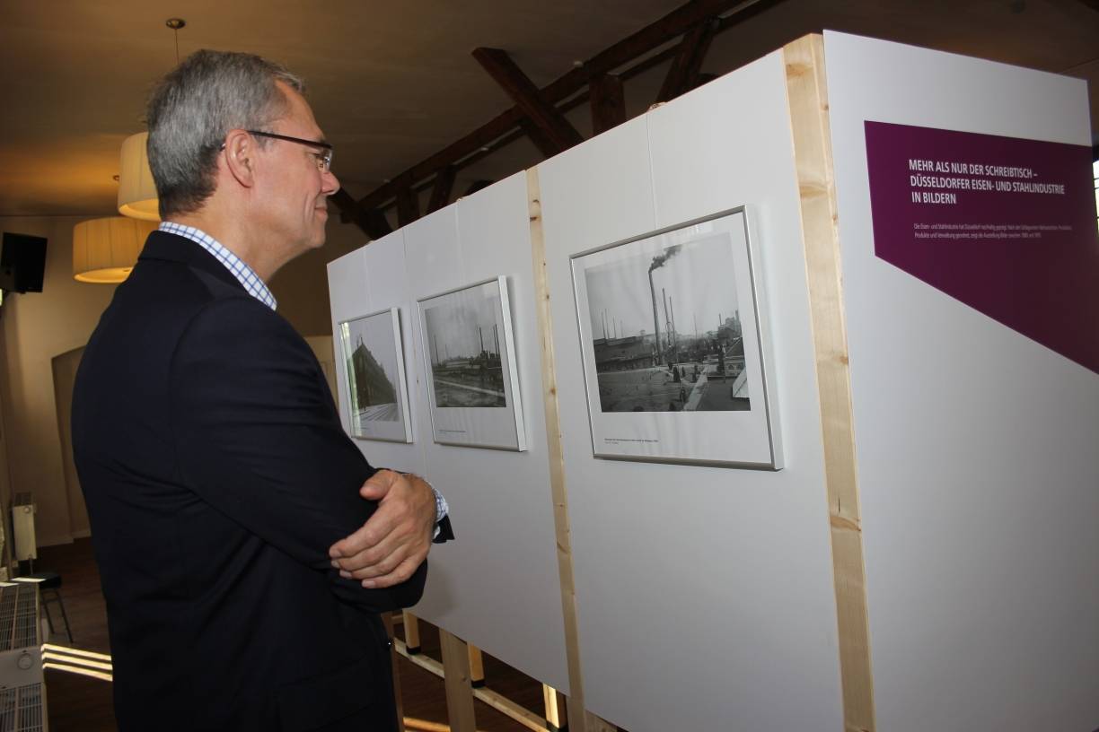  Dr. Ulrich Menne von Vallourec lächelt vor einem historischen Foto der Mannesmann Röhrenwerke. 