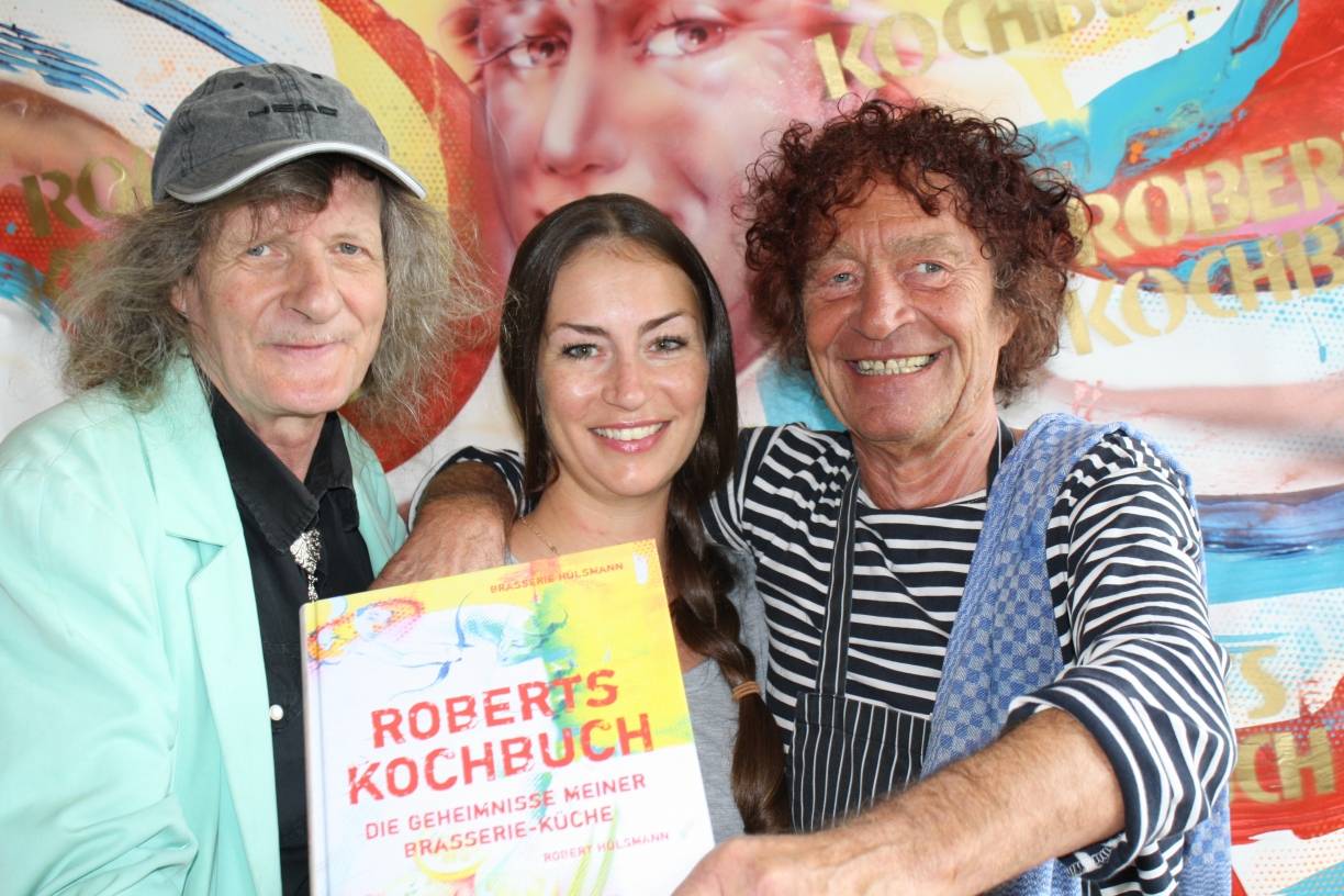  Robert Hülsmann (r.), seine Tochter Jennifer und der Künstler Joe Brockerhoff (l.) stellen das neue Kochbuch vor. 