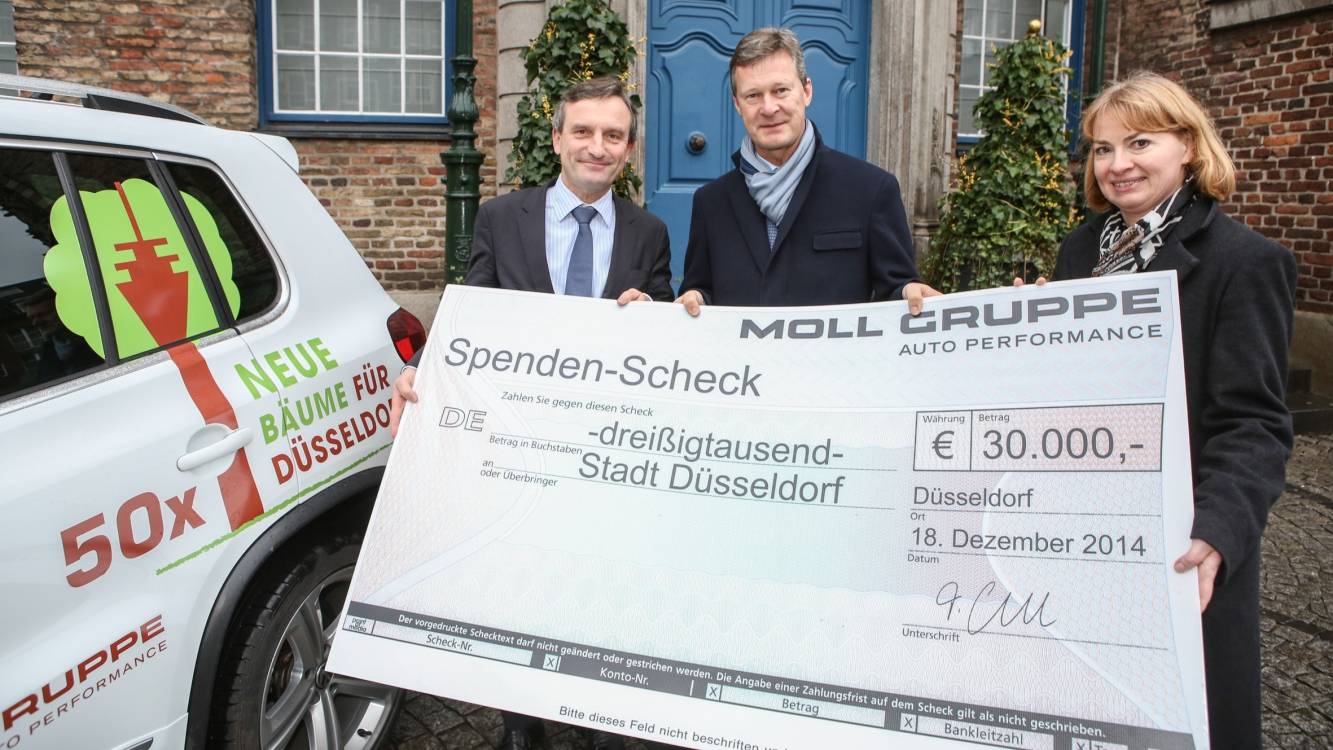  Oberbürgermeister Thomas Geisel nimmt den symbolischen Scheck über 30.000 Euro aus den Händen von Timm Moll und Yvonne Peters, Geschäftsführer der Moll Gruppe — Auto Performance entgegen. Das Geld wird für die Anpflanzung von 50 neuen Bäumen verwendet. 