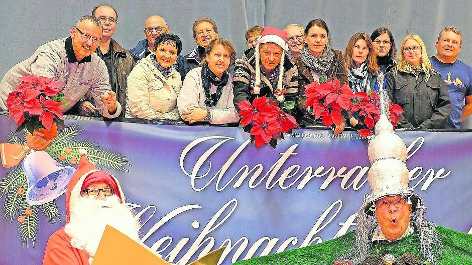  „Weihnachtsbaum“ Hermann Schmitz (rechts) moderiert das Bühnenprogramm beim Unterrather Weihnachtsmarkt. Neben ihm „Nikolaus“ Dieter Risse, dahinter Mitglieder der „Einkaufs-Trümpfe“ mit ihrem Vorsitzenden Frank Schöffel (rote Kappe). 