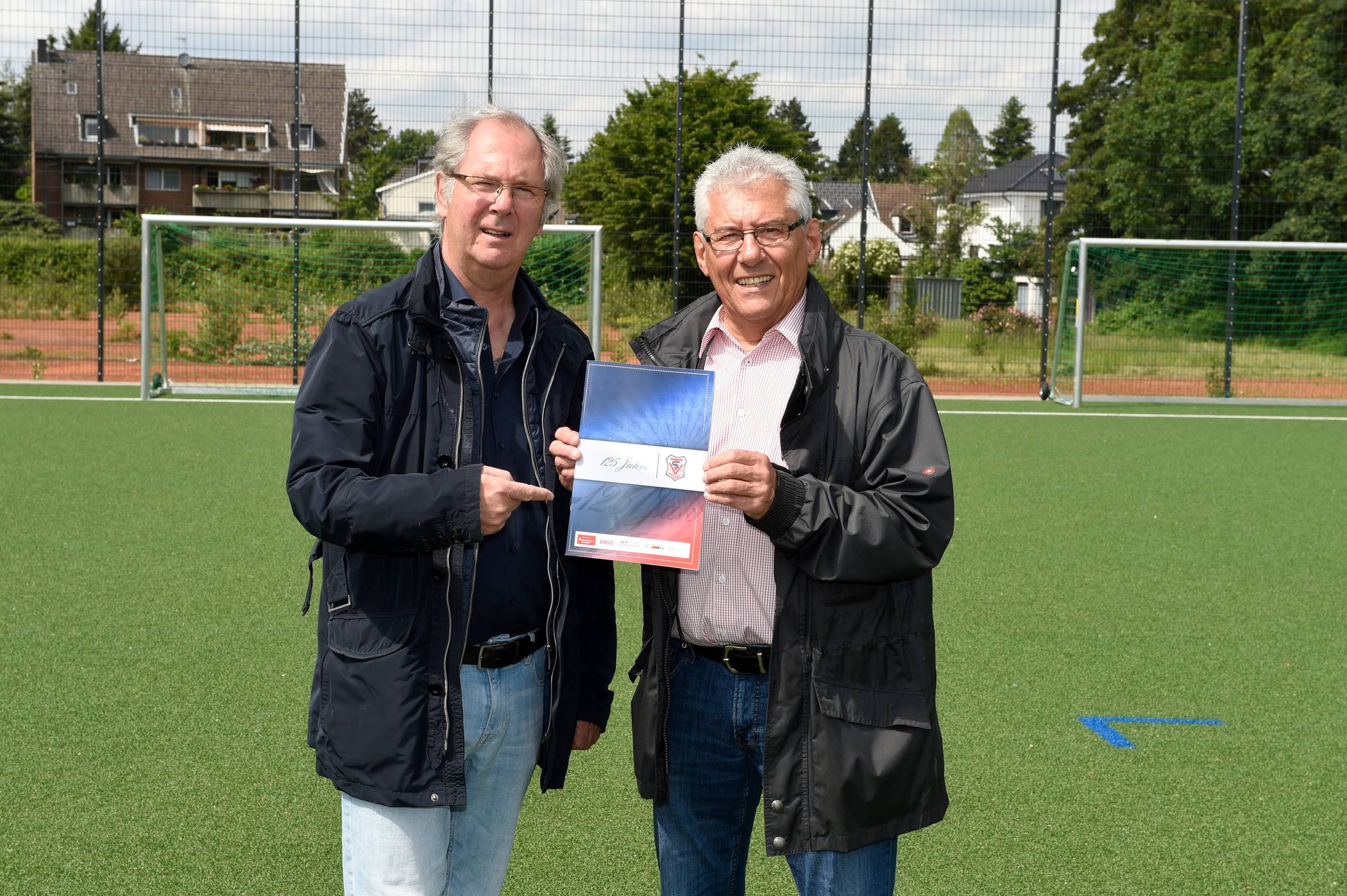  Vereinsvorsitzende Peter Wallscheid (l.) und Friedhelm Gutowski mit einem Exemplar der knapp 70-seitigen Jubiläums-Broschüre zum 125-jährigen Klub-Geburtstag auf der neuen Fußballanlage des TSV Urdenbach. 