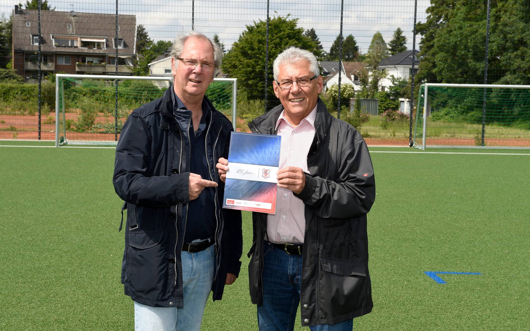  Vereinsvorsitzende Peter Wallscheid (l.) und Friedhelm Gutowski mit einem Exemplar der knapp 70-seitigen Jubiläums-Broschüre zum 125-jährigen Klub-Geburtstag auf der neuen Fußballanlage des TSV Urdenbach. 